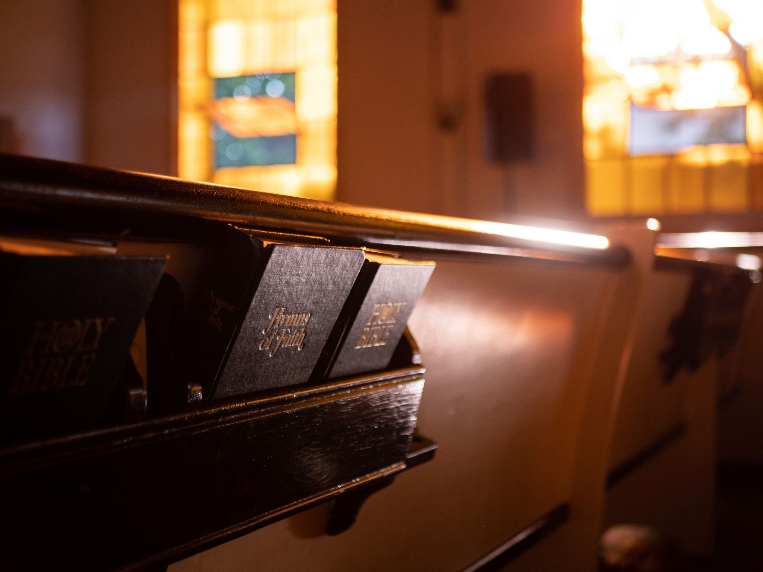 Gesangbücher in einer Kirchenbank, warmes Buntglaslicht