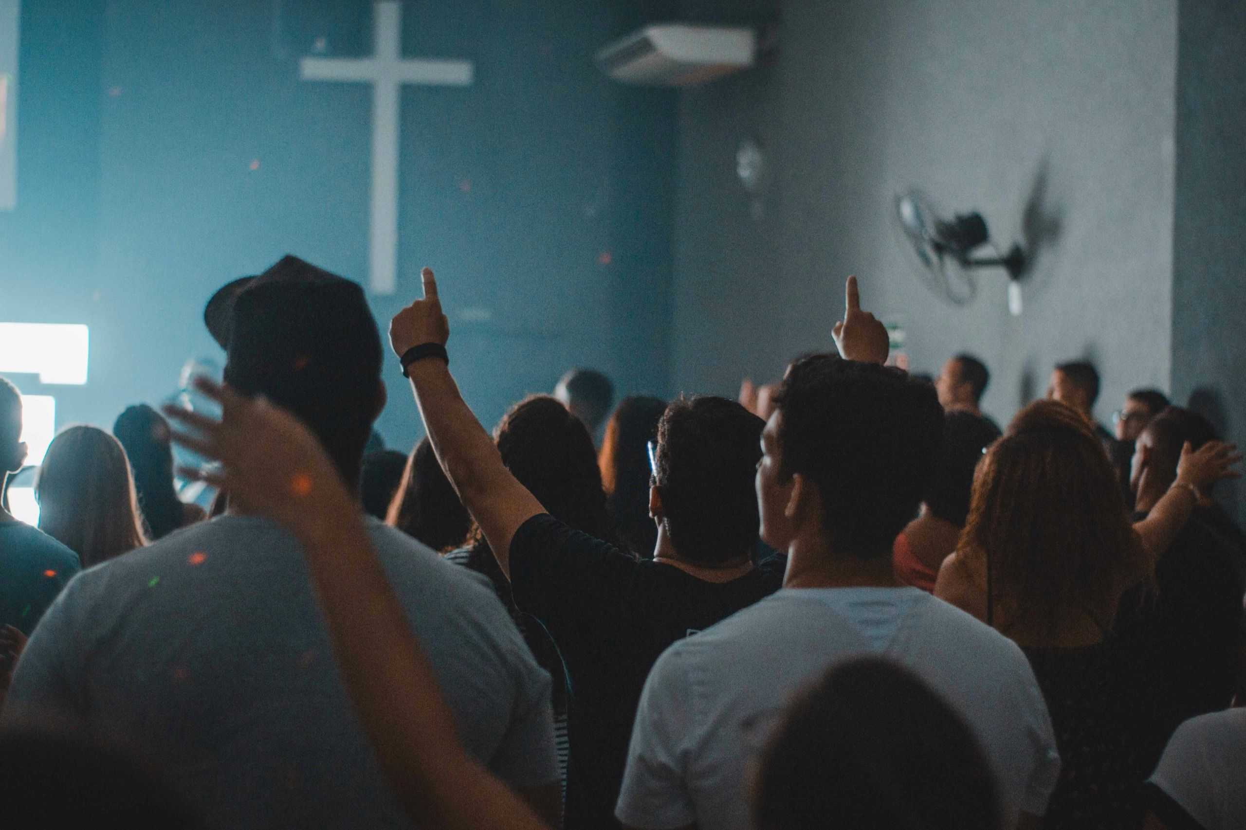 Junge Gemeinde beim Worship, erhobene Hand vor beleuchtetem Kreuz